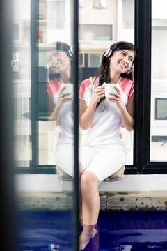 印尼妇女在家喝咖啡时戴着耳机听音乐