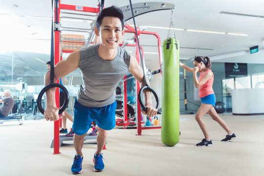在一个时髦的健身中心，一个拥有现代功能训练设备的快乐健康的年轻人在常规训练中戴着体操环进行锻炼