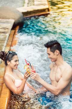 暑假期间，一个英俊的年轻人一边在时髦的游泳池里喝着美味的鸡尾酒，一边和一个迷人的女人调情