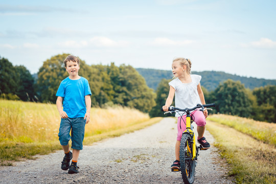 小男孩和小女孩在土路上散步和骑自行车