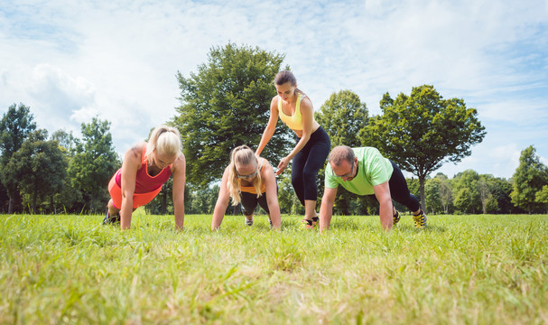 在草地上由健身教练指导下，一家人在大自然中做俯卧撑