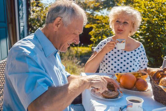 夏天，年长的女人和男人坐在花园里吃早餐，吃面包卷，喝咖啡