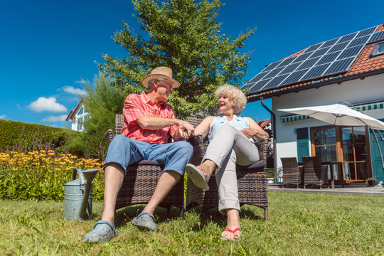 在阳光明媚的夏日里，一对幸福的相爱的老年夫妇坐在椅子上，在家里的花园里一起放松