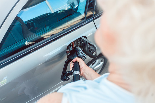 在加油站为汽车加油时，一位老妇人手拿着加油泵的侧面特写镜头