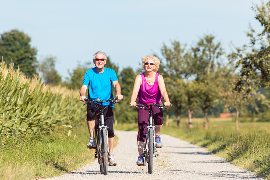 在一个阳光明媚的夏日，一对活跃的老年夫妇骑着自行车在乡村享受退休生活的全景