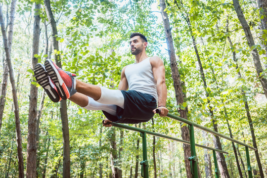 健美男子在森林户外健身房用双杠做腹部运动