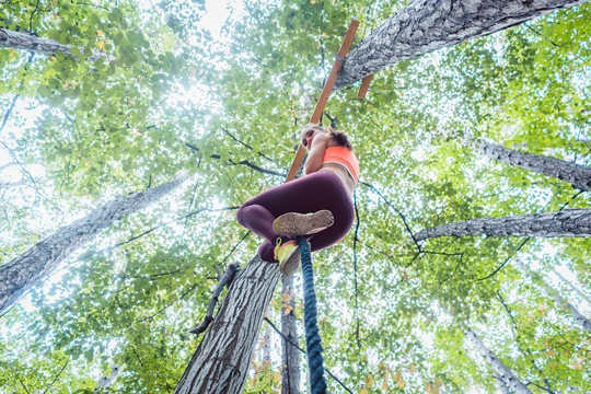 非常健康和运动型的女人攀爬绑在树上的绳子