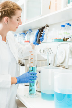 一位年轻的女医生在实验室里测试化学物质，她身穿实验室工作服，戴着手套