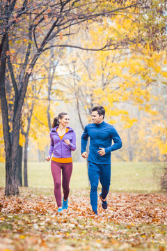 在一个有着五颜六色树叶的秋天公园里，男人和女人在做健身运动