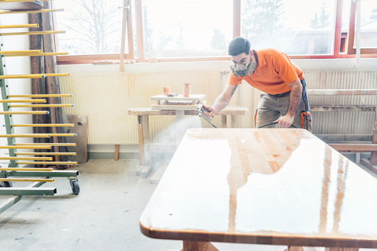 木匠用呼吸保护装置在他工作的桌子上喷清漆