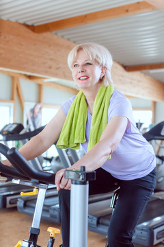 高级女性在现代健身房骑自行车锻炼身体