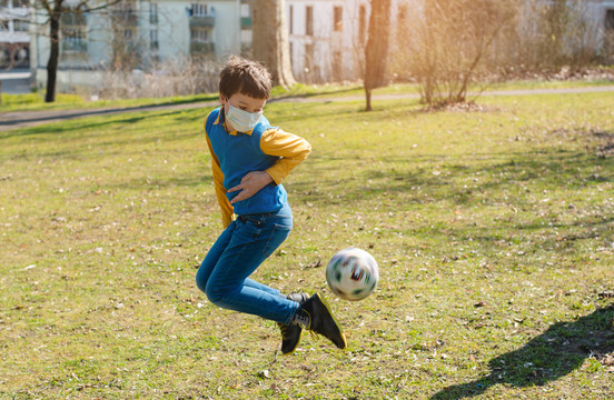 男孩在公园踢足球，尽管CVID-19危机仍保持活跃