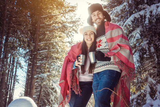 在寒冷的冬日，女人和男人在雪树中用热茶取暖