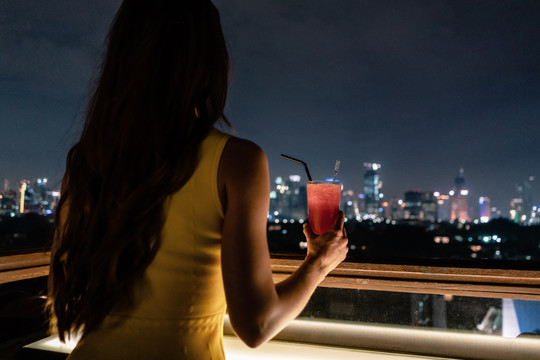在屋顶露台上喝饮料的女人俯瞰着城市的天际线