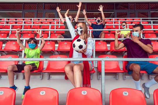 戴着面具在体育场观看社交距离措施下足球比赛的球迷