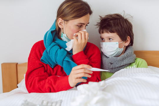 母亲和儿子因感染病毒躺在床上看体温计