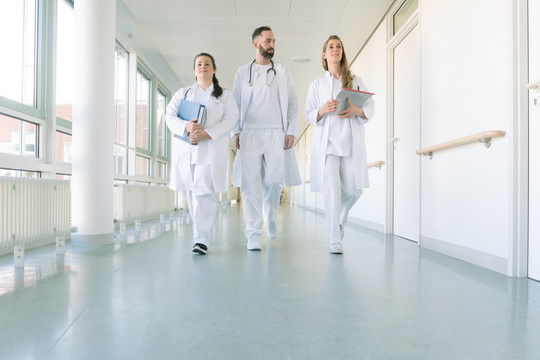 医生们，两个女人和一个男人，在医院里沿着走廊走着