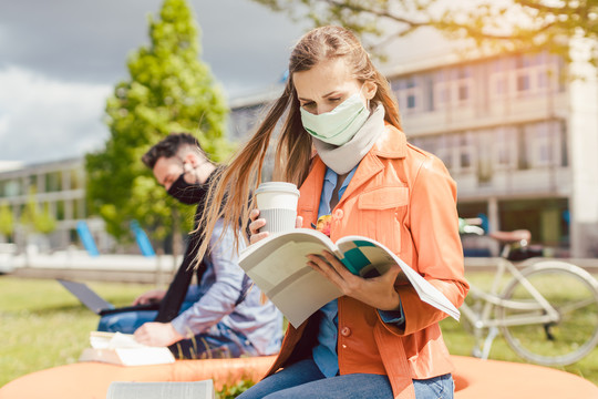 大学校园里的一名女学生在使用笔记本电脑时正在学习戴口罩