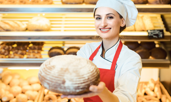 在面包店，一名女售货员拿着围裙，向镜头展示新鲜面包