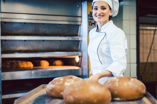 面包师妇女在铁锹上展示刚烤好的面包，几乎可以闻到新鲜的味道