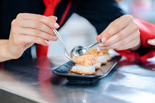 女厨师在一个黑色陶瓷盘子里给完成的开胃菜调味