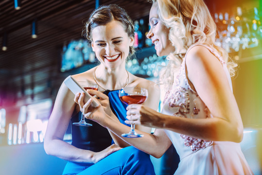 两个女人在酒吧里看手机玩得很开心
