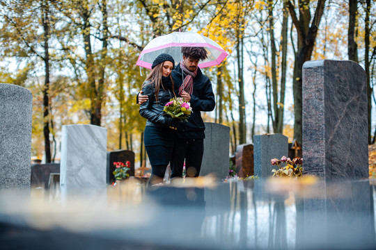 一对夫妇站在坟墓之间，在墓地悼念一位逝去的爱人
