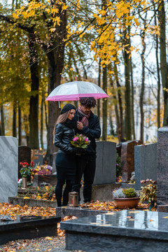 男人和女人在一个有鲜花和秋天落叶的墓地上