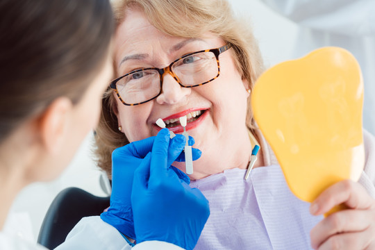 牙科医生在牙齿漂白前向老年患者展示牙齿颜色样本