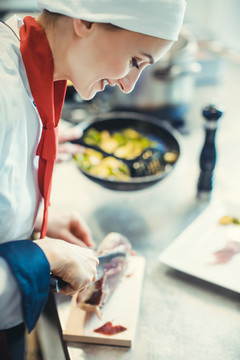 厨师在高级餐厅的厨房里为一道菜切火腿，背景是一盘食物