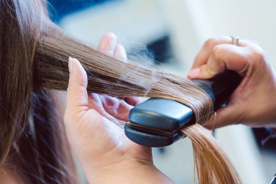 美发师在女顾客的头发上使用扁铁，特写镜头