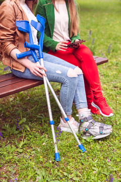 两个女人，一个健康，一个扭伤了脚，坐在公园的长凳上