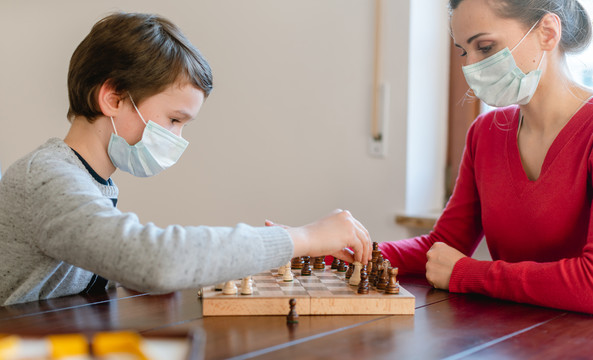 冠状病毒危机期间母亲和孩子戴着口罩在家下棋
