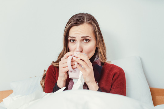 一位喝着热茶和感冒的妇女躺在床上发烧