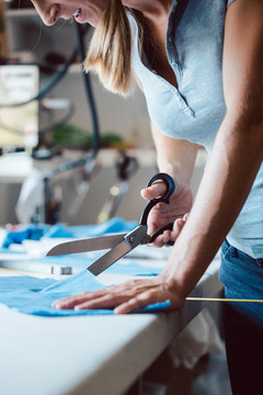 在工作室里，一名妇女在裁缝桌上用裁缝剪刀剪布料