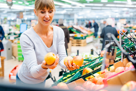 一名妇女手拿苹果在超市货架上测试新鲜水果