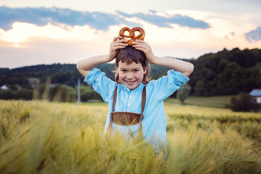 年轻的巴伐利亚男孩拿着椒盐卷饼在草地上看着摄像机