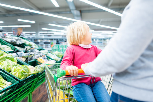母亲和蹒跚学步的孩子在超市里用购物车购买食品杂货