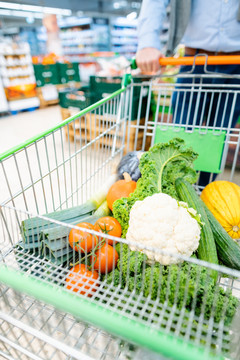 一名男子在超市购物，推着手推车，里面装满了蔬菜和杂货