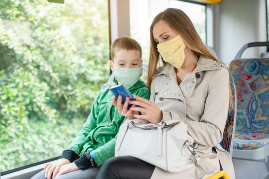 在冠状病毒危机期间，一名妇女和她的儿子在公共汽车上看电话