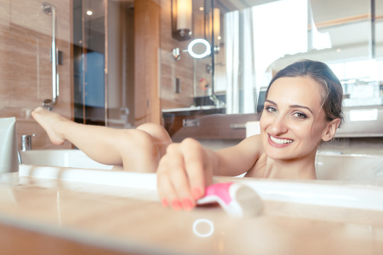 在酒店浴缸里洗澡的女人抓着剃须刀去腿毛