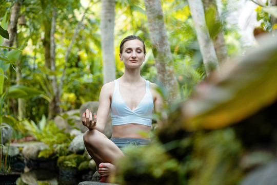 在热带丛林中坐在石头上做瑜伽的女人