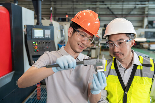 两个工程师穿保护工作服戴着安全帽在工厂工作