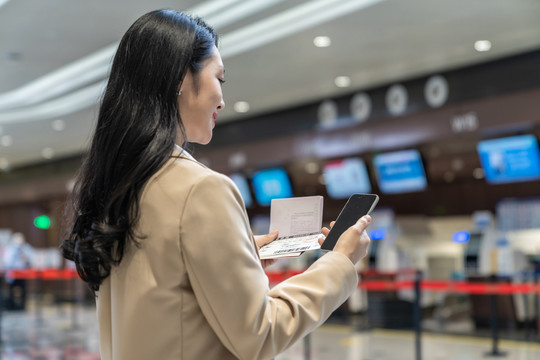 商务女士拿着护照在机场使用手机