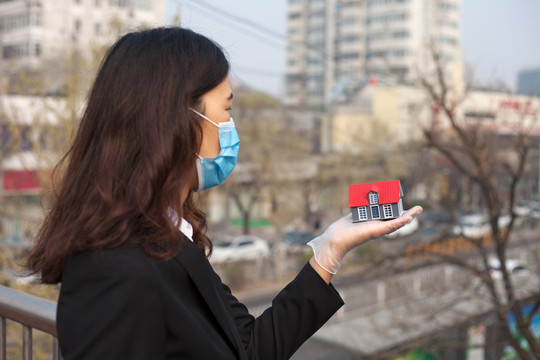 戴口罩的女销售手托房子模型