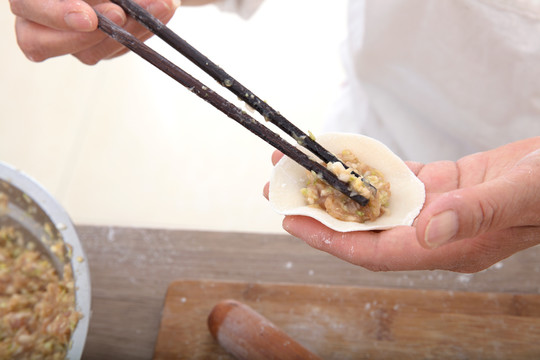 筷子夹着肉馅放进饺子皮里包饺子