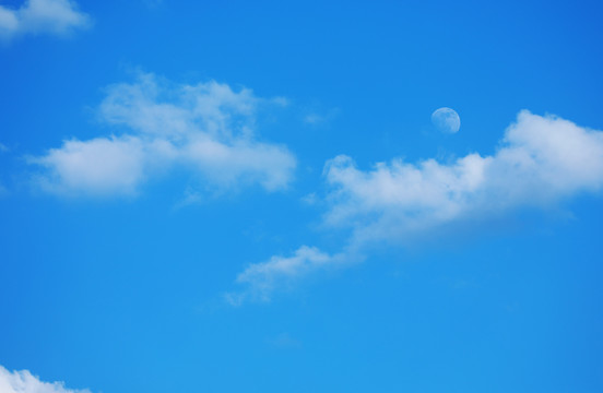傍晚天空中月亮挂在蓝天白云