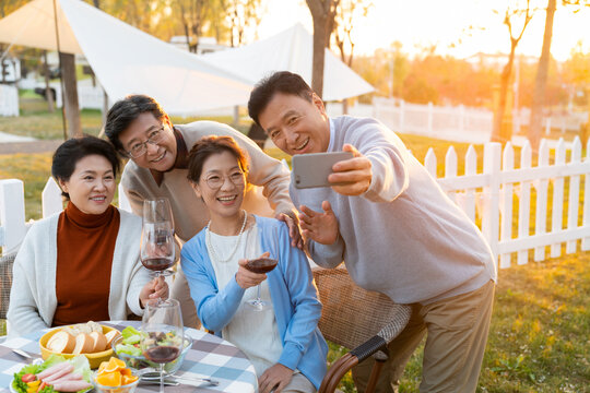 夕阳下中老年朋友在庭院里聚会喝酒拍照片