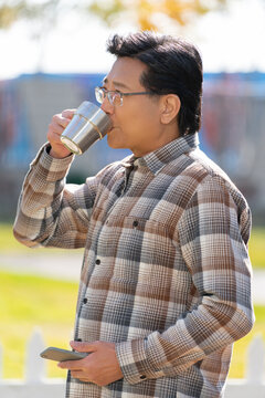 一个老年男人站在露营院子里拿着手机喝咖啡