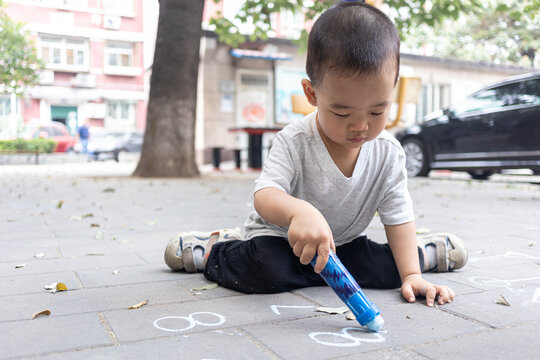 一个小男孩坐在地上用粉笔写字